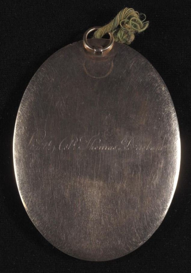 The shiny gold reverse side of a locket portrait, with the following engraved on it: Lieutt Coll Thomas Brisbane.