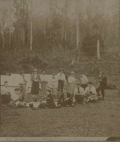 An old photograph of people from the late 1800s dressed in pants, having a picnic.