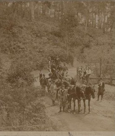 An old photograph of people from the late 1800s walking along a trail with horses and a wagon.